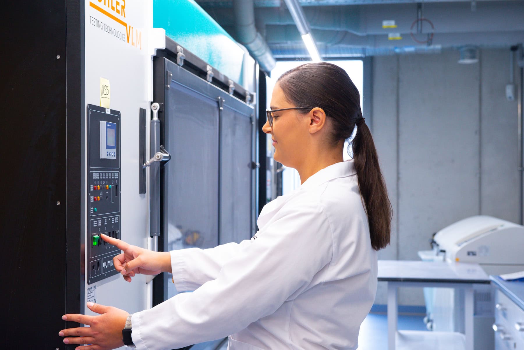 A laboratory technician operates a test chamber for cyclic corrosion testing